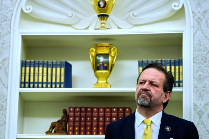 Sebastian Gorka listens as President Donald Trump speaks with reporters after signing executive orders in the Oval Office of the White House, April 23, 2025, in Washington. [AP Photo/Alex Brandon]